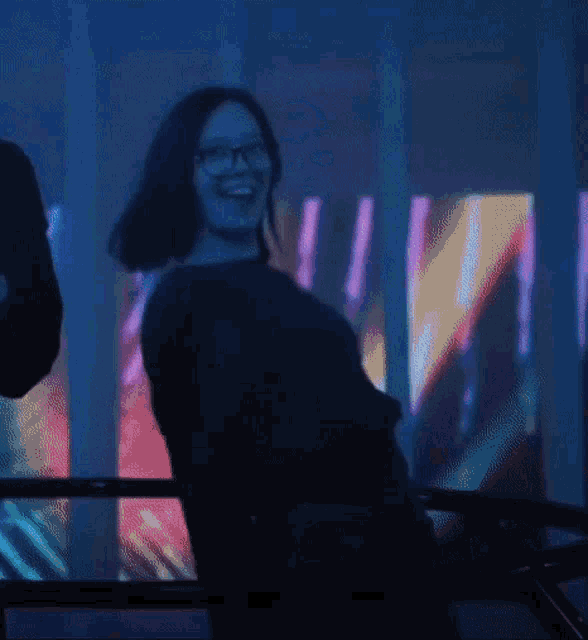 a woman wearing glasses is dancing in front of a colorful wall