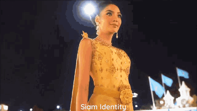 a woman in a yellow dress is standing in front of a siam identity sign