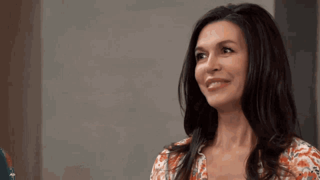 a woman in a floral shirt is smiling while looking at the camera .