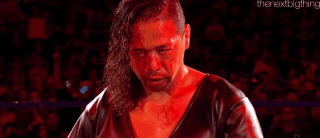 a wrestler with blood on his face is standing in a ring with his eyes closed .