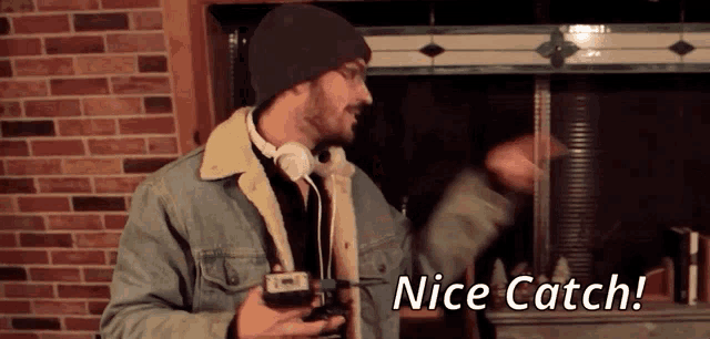 a man wearing headphones and a denim jacket is holding a camera and says nice catch