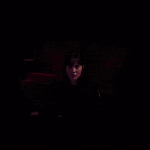 a woman is sitting in a dark room with a red light behind her