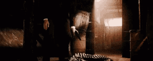 a man in a suit is standing next to a zebra laying on the floor in a dark room .