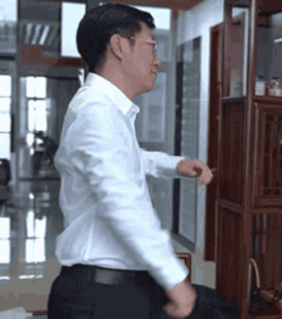 a man in a white shirt and black pants is sitting in front of a bookshelf .