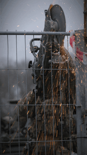 a man is cutting a metal fence with a circular saw and sparks are flying