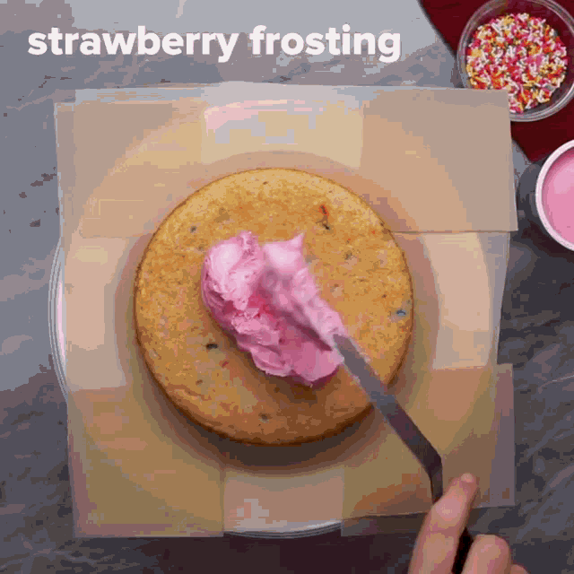 strawberry frosting is being applied to a cake with a spatula