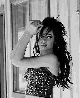 a black and white photo of a woman in a corset standing in front of a window .