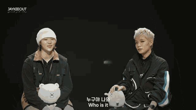 two young men are sitting next to each other and one of them is holding a stuffed animal with the words who is it on it
