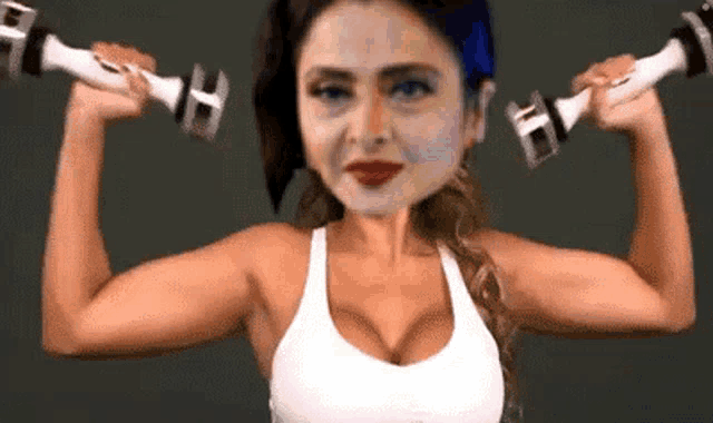 a woman in a white tank top is holding a pair of dumbbells in her hands .