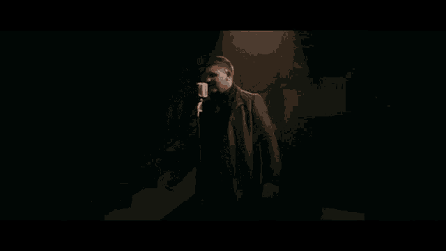 a man in a suit is standing in front of a microphone in a dark room .