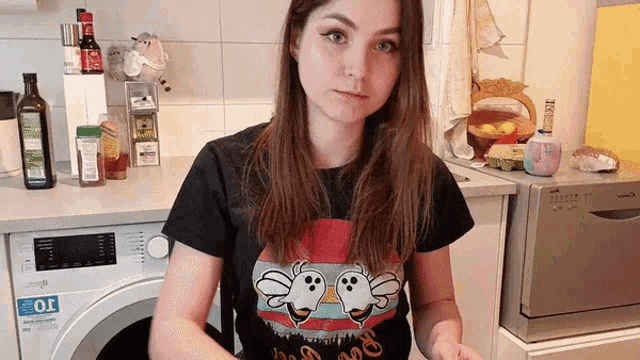 a woman wearing a t-shirt with ghosts on it is standing in a kitchen