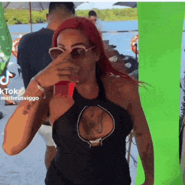 a woman with red hair is drinking from a red cup while wearing sunglasses