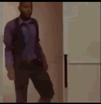 a man in a purple shirt and black pants is standing in front of a white refrigerator .