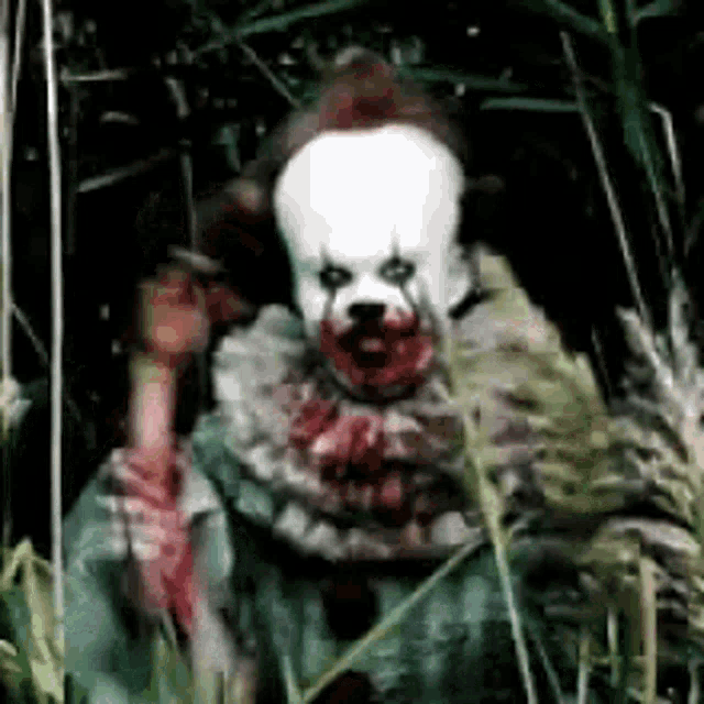 a scary clown is standing in the grass with blood on his face .