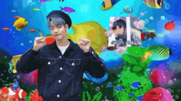 a man in a denim jacket and beret is standing in front of a coral reef surrounded by fish .