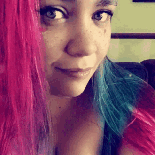 a woman with pink and blue hair is smiling and looking at the camera
