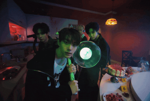a group of young men are standing around a table with plates of food and a cake with the number 6 on it