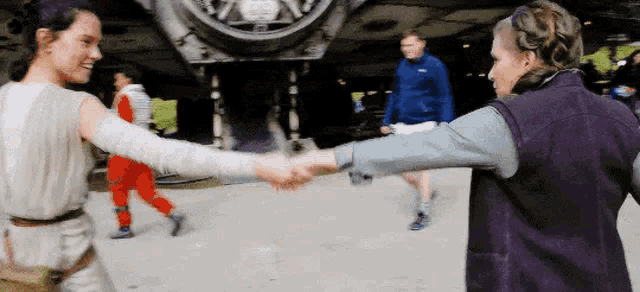 a couple of women are shaking hands in front of a giant vehicle .