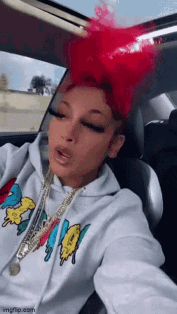 a woman with red hair is sitting in a car wearing a white hoodie and a necklace .