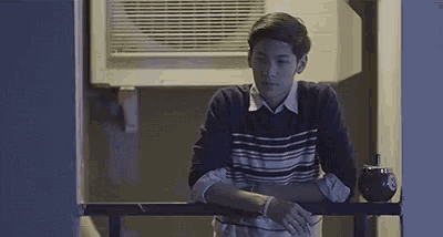 a young man is sitting on a balcony with his hands on the railing .