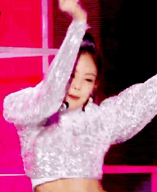 a woman in a white sequined crop top is dancing with her arms outstretched .