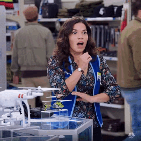 a woman is standing in front of a display of drones in a store and making a surprised face .