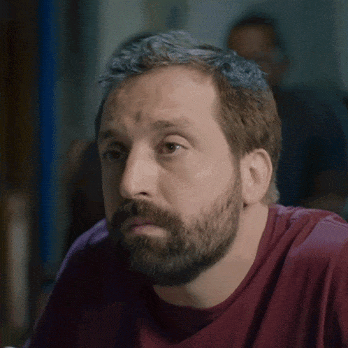 a man with a beard wearing a red shirt is looking at something