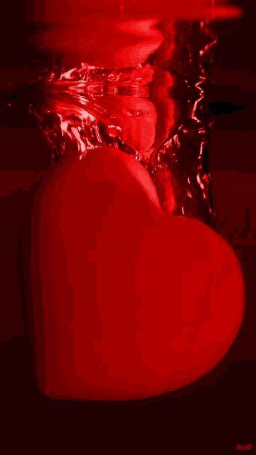 a red heart is floating in a glass of water with a splash