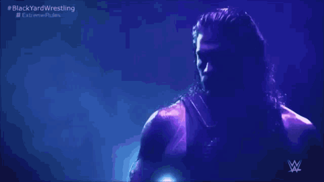 a wrestler is standing in front of a purple background with the words blackyardwrestling written on it .