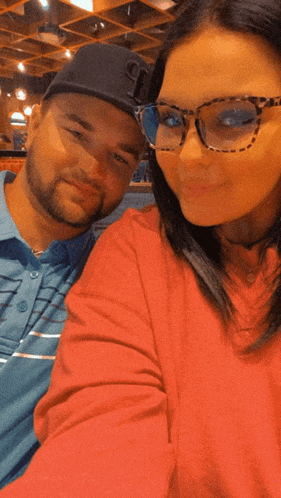 a man and a woman are posing for a picture and the woman is wearing glasses and a hat that says t on it