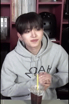 a man in a hoodie is sitting at a table with a cup of coffee .