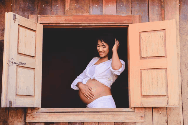 a pregnant woman looks out of a wooden window with shutters open and a photo by dan hene