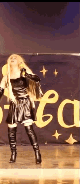 a woman in a black dress and boots is singing into a microphone