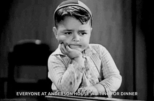 a black and white photo of a sad little boy sitting at a table waiting for dinner .