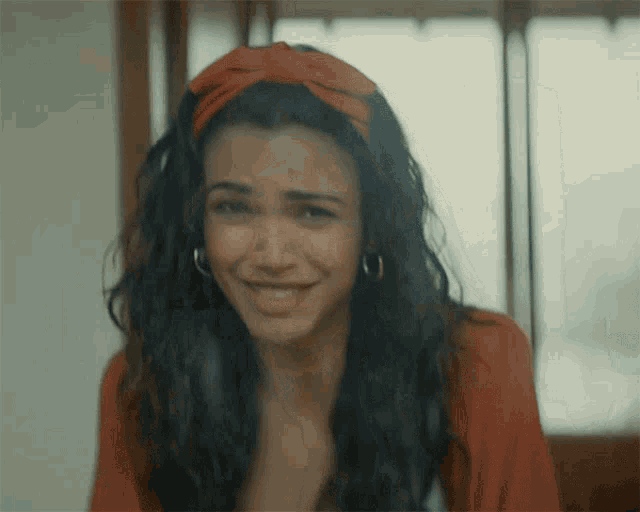 a woman wearing a red headband and hoop earrings smiles for the camera