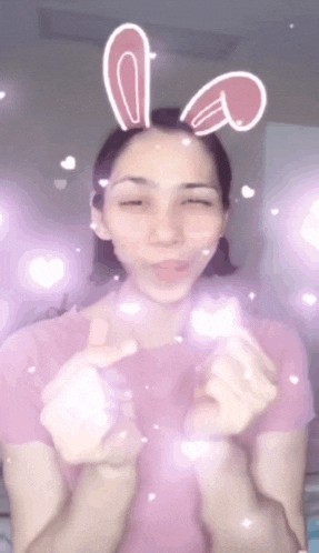 a woman wearing bunny ears and making a heart sign