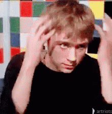 a man in a black shirt is scratching his head with his hands