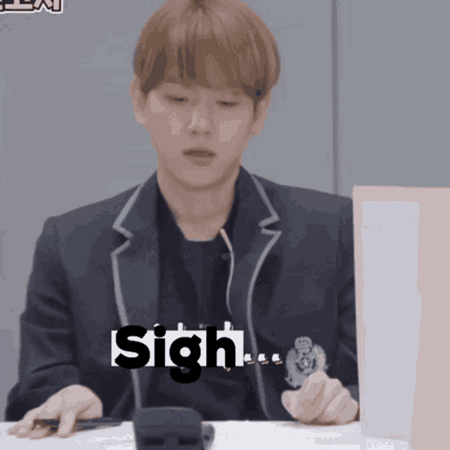a young man in a suit is sitting at a table with the word sigh written on his face