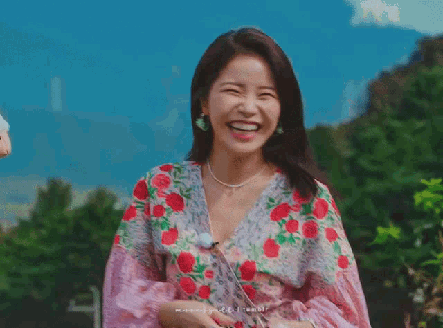 a woman wearing a pink and white floral dress is clapping her hands