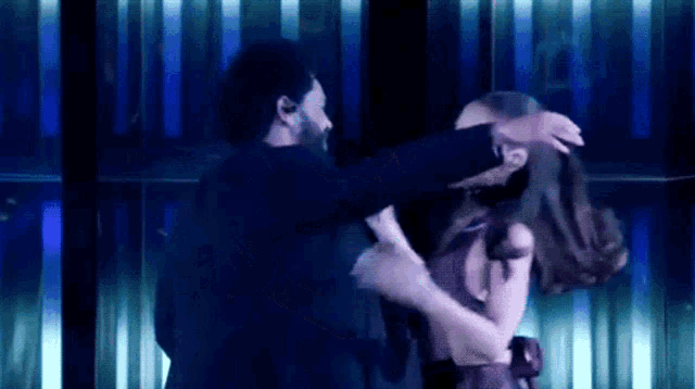 a man is hugging a woman in a dark room with blue lights behind them