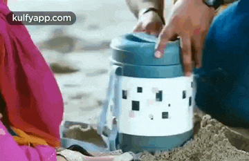 a man and a woman are sitting on a beach holding a thermos .