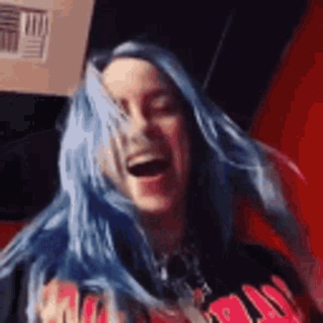 a woman with blue hair is laughing with her mouth open in a room .
