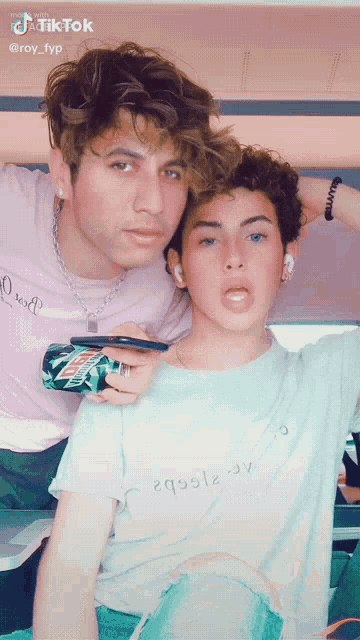two young men are posing for a picture and one of them is holding a can of mountain dew