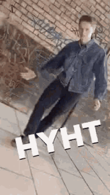 a man in a denim jacket and jeans is standing on a sidewalk .