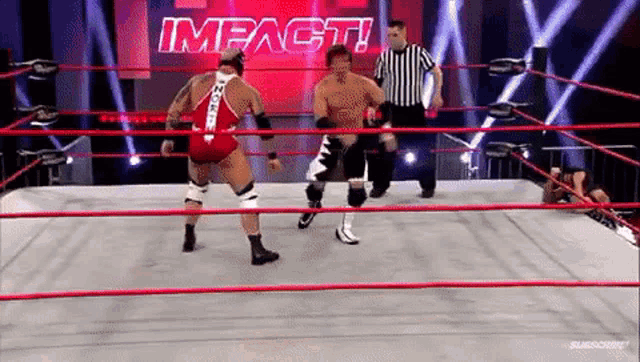 two men are wrestling in a wrestling ring with a referee in the background .