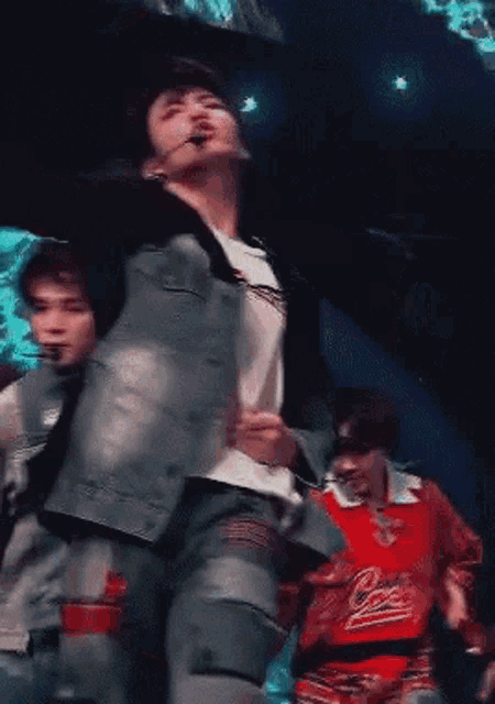 a man in a blue jacket is dancing on a stage with other people