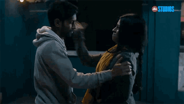 a man and a woman are hugging each other in front of a sign that says jio studios .