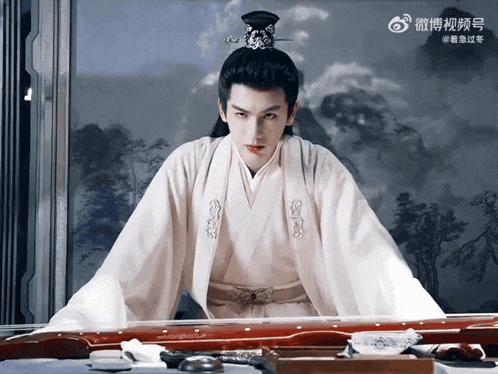 a man in a white kimono is sitting in front of a painting with chinese characters on it