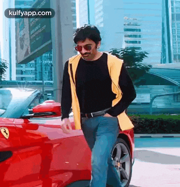 a man wearing sunglasses and a yellow vest is standing next to a red ferrari .