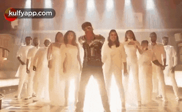 a man is dancing with a group of people in white clothes on a stage .